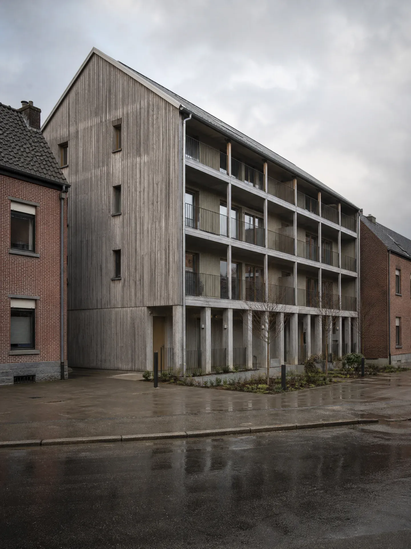 Immeuble de logements en bardage de mélèze grisé, entre deux maisons en brique